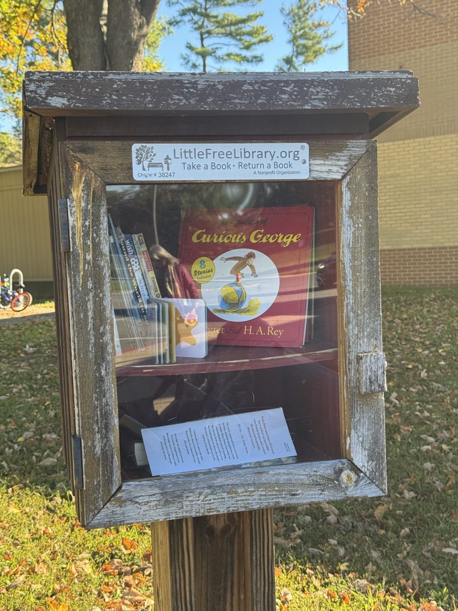 Thunder Hill's Little Free Library: a weathered wooden book box on a post in front of the school, with a glass door showing children's books including Curious George, and a plaque reading LittleFreeLibrary.org, Take a Book, Return a Book, Charter #38247.